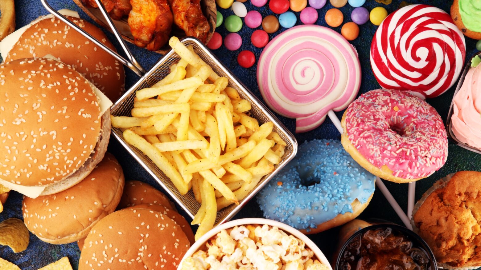 An array of ultra-processed foods including burgers, popcorn, fries, donuts, and candy