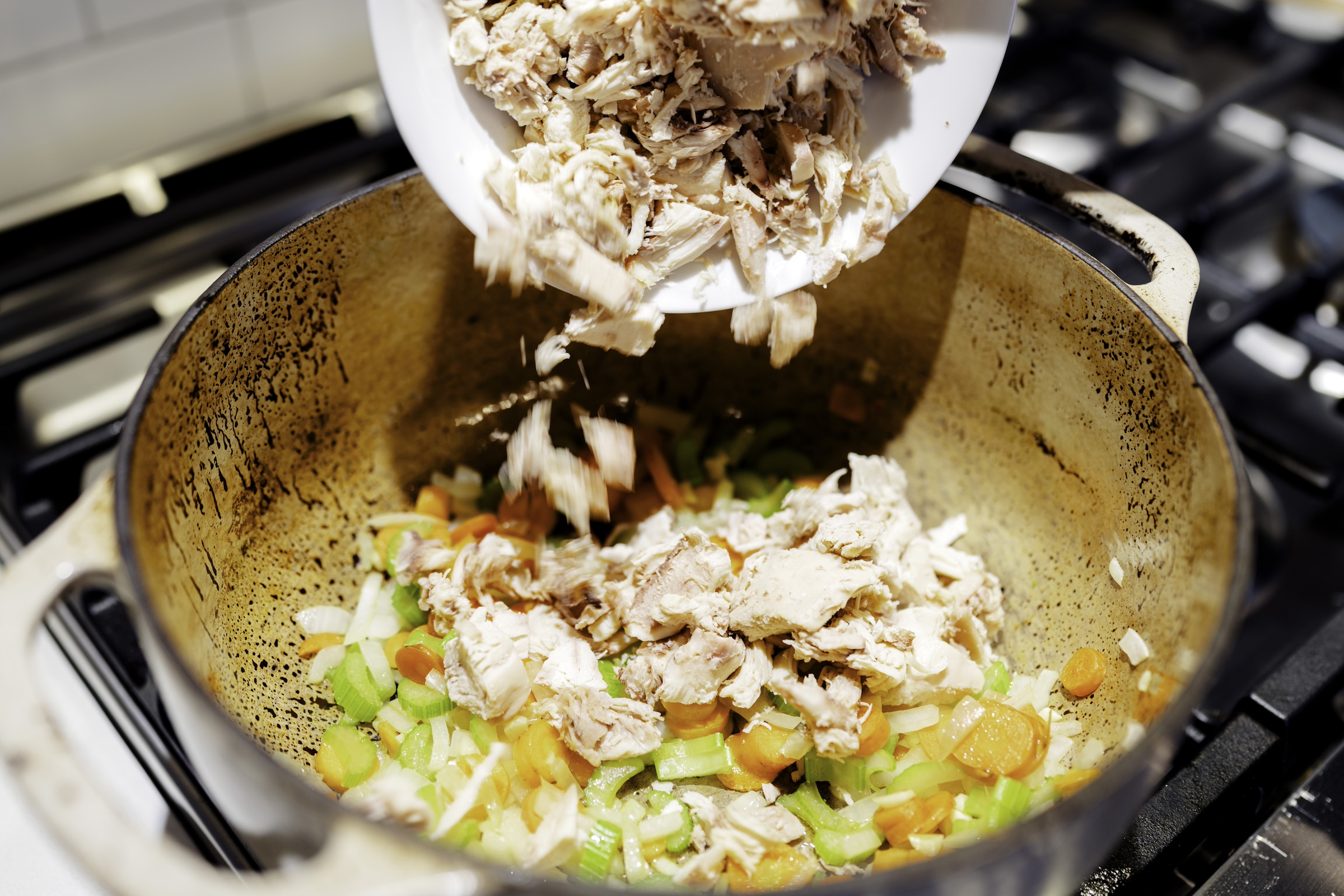 Pouring the shredded chicken into the mustard chicken soup. 