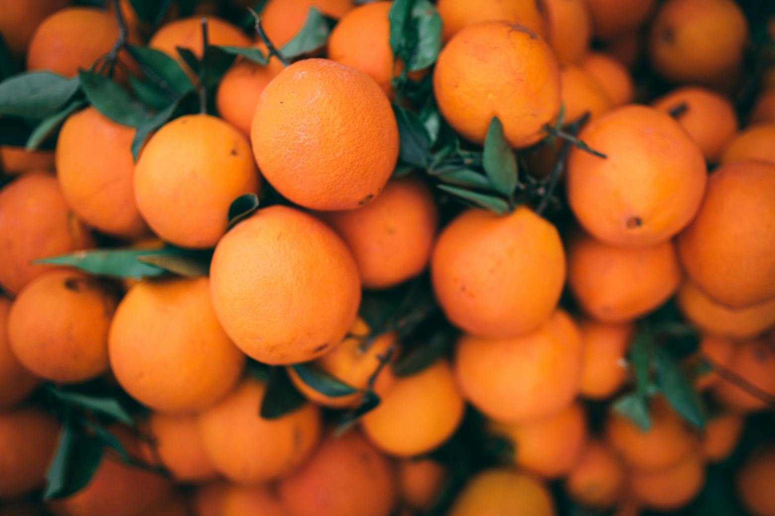 A vibrant pile of fresh oranges with attached green leaves.