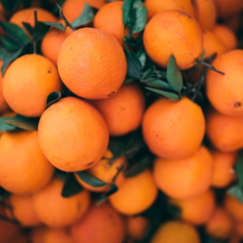 A vibrant pile of fresh oranges with attached green leaves.