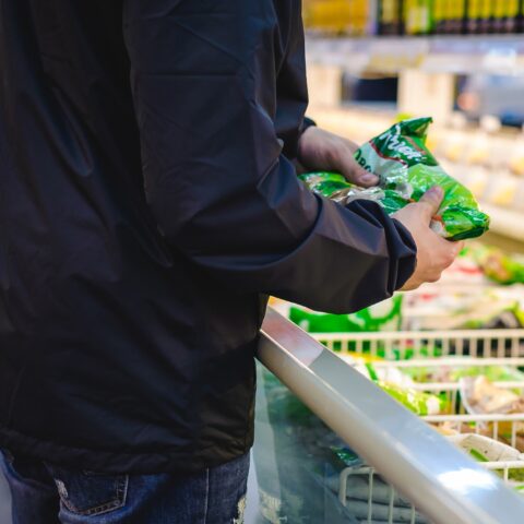 Close-up of a man holding a bag of frozen vegetable while standing in front of a frozen food section