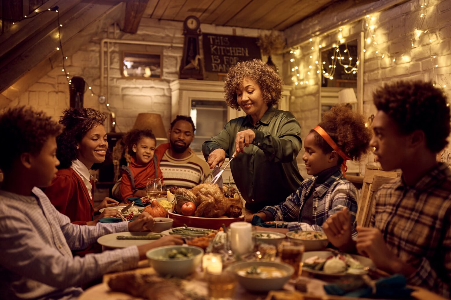 A family sits around the table for a holiday dinner, with the mother cutting into a roast turkey