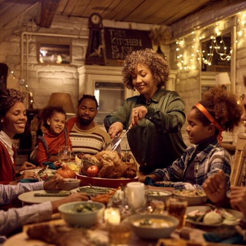 A family sits around the table for a holiday dinner, with the mother cutting into a roast turkey