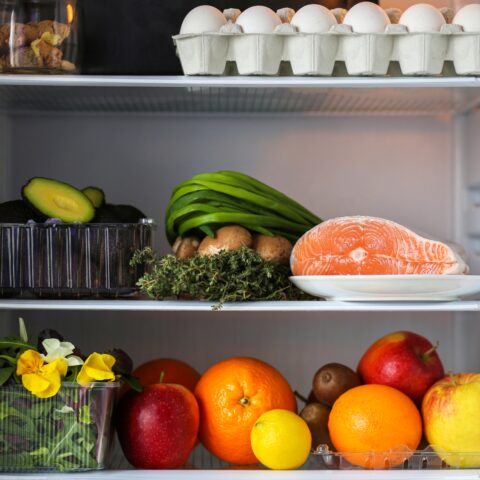 An orderly fridge with fresh meat, eggs, and produce on display.