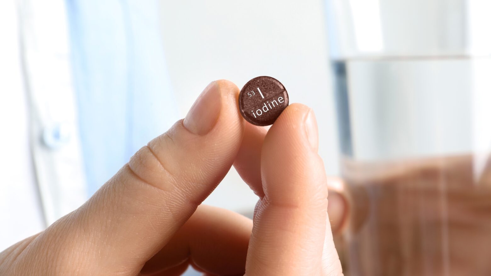 Closeup of a hand holding a small brown iodine tablet