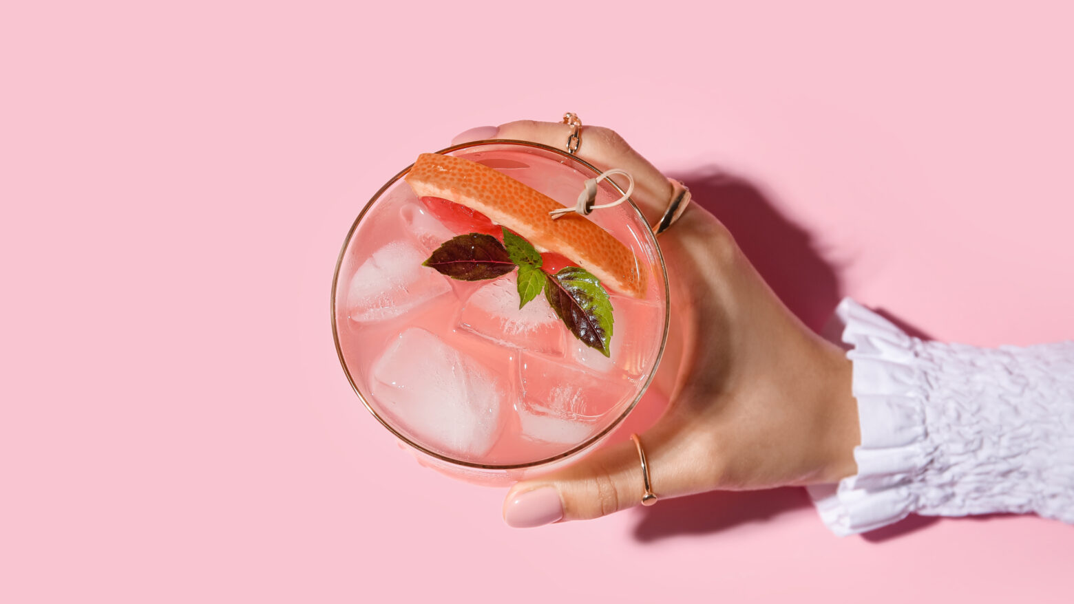 Above shot of a female hand holding a pink cocktail over a pink background