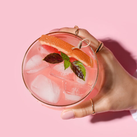 Above shot of a female hand holding a pink cocktail over a pink background