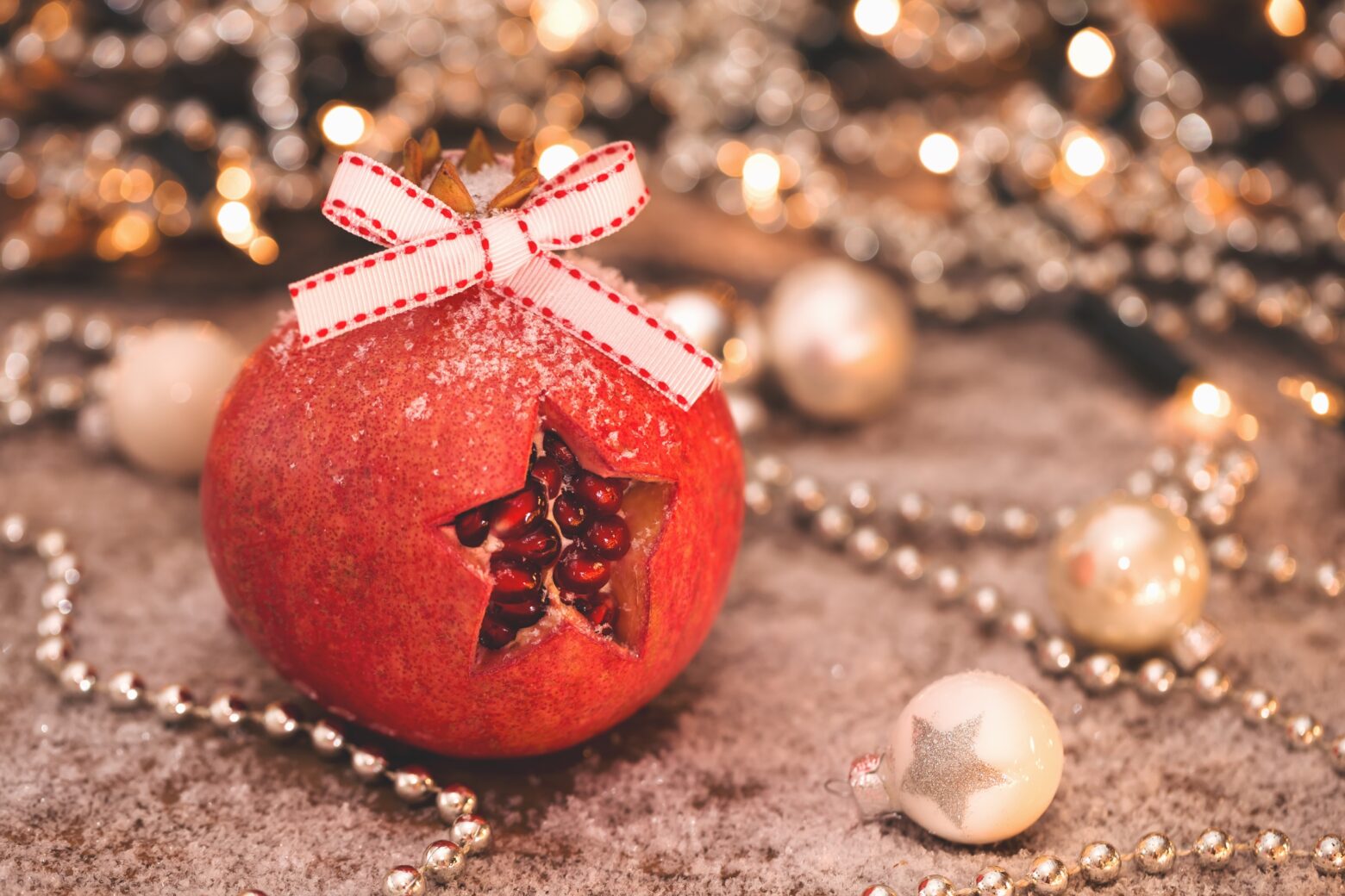 A pomegranate with a star shape cut into the rind, sitting among white and gold holiday decorations