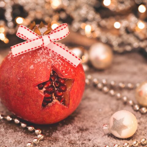 A pomegranate with a star shape cut into the rind, sitting among white and gold holiday decorations