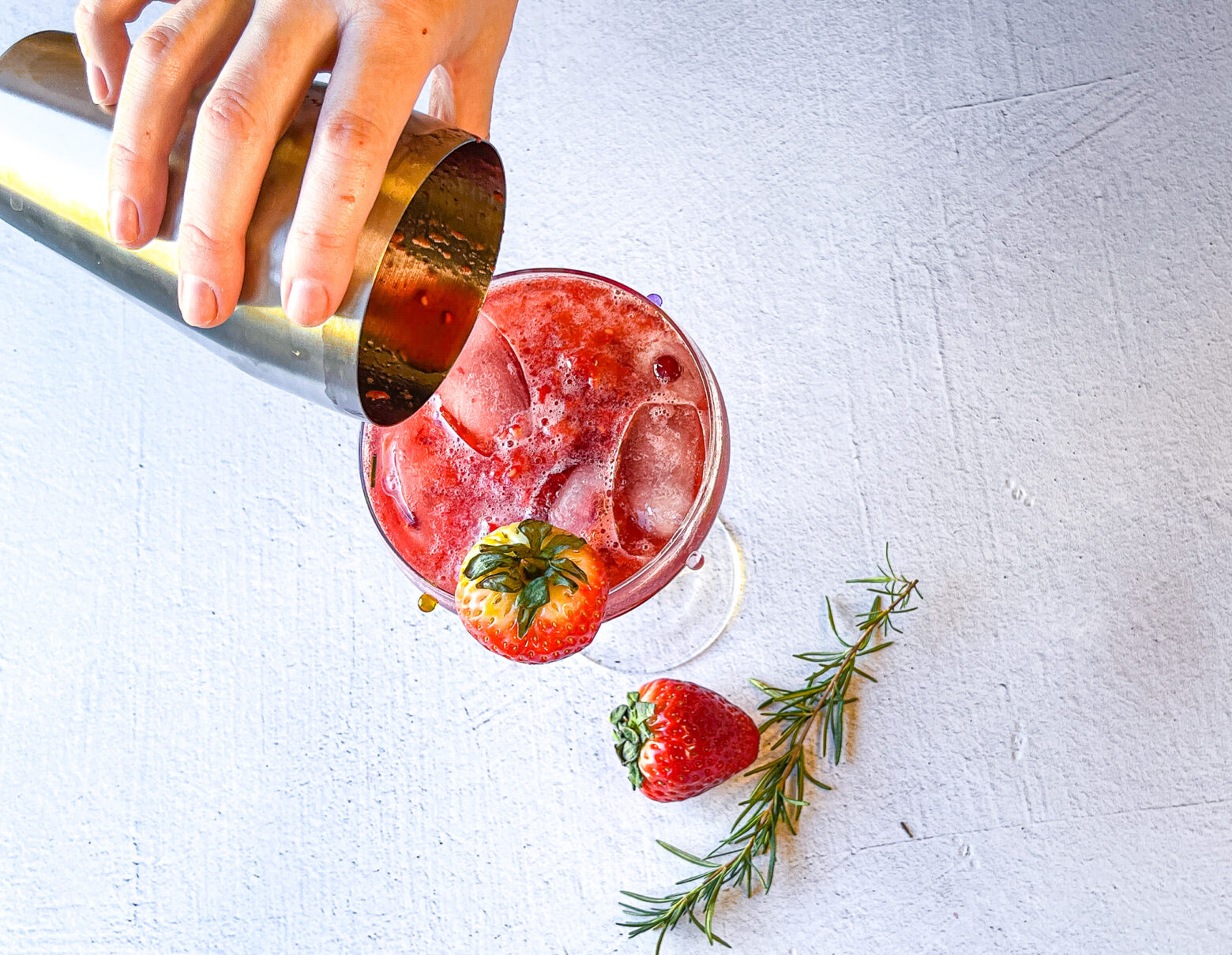 Pouring strawberry sour mocktail from the cocktail shaker into the martini glass.