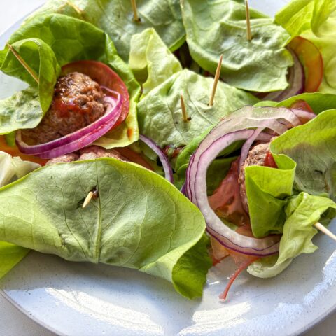 Finished bunless sliders on a plate in lettuce wraps.