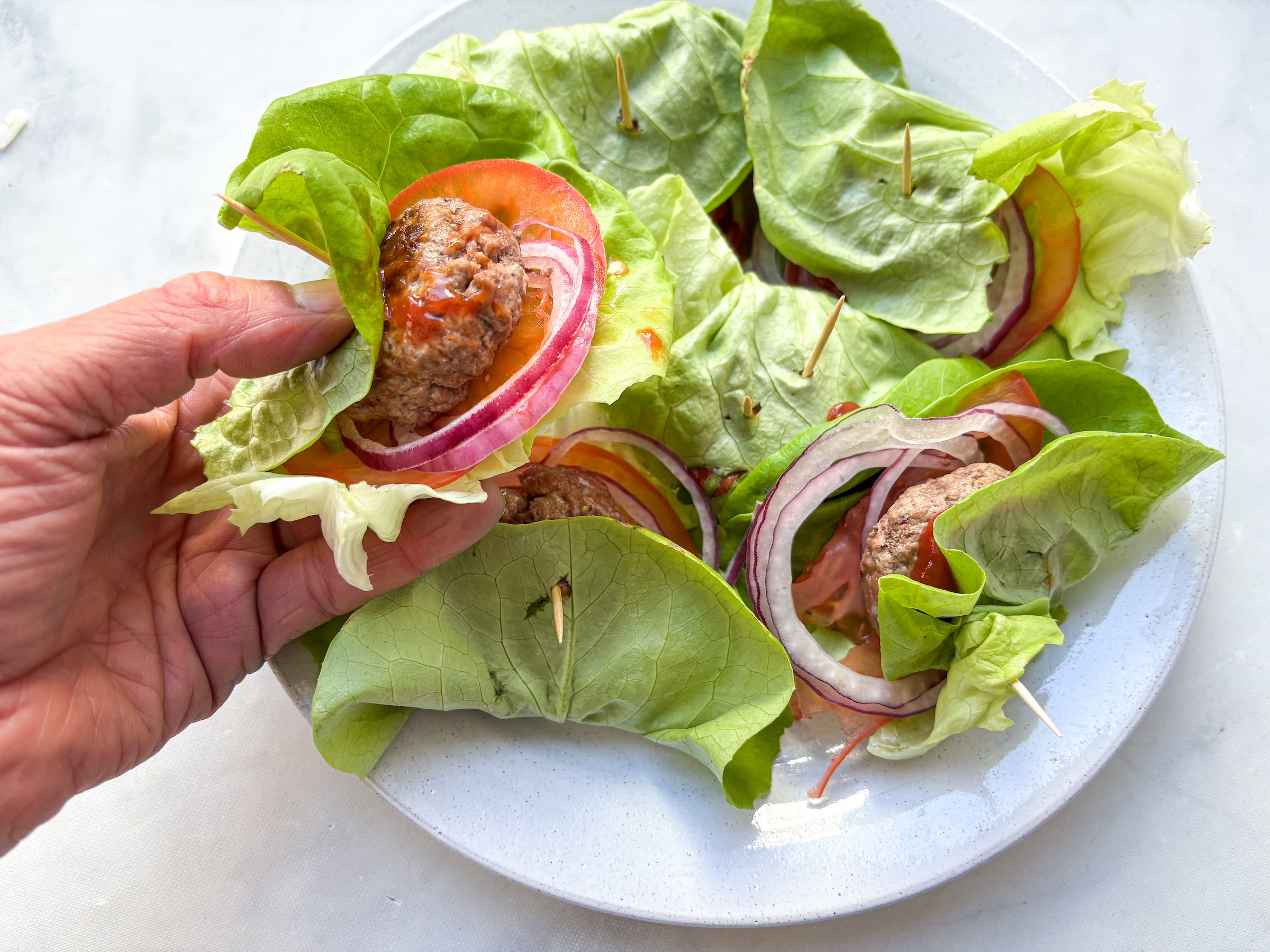 A hand holding a bunless sliders that are finished. 