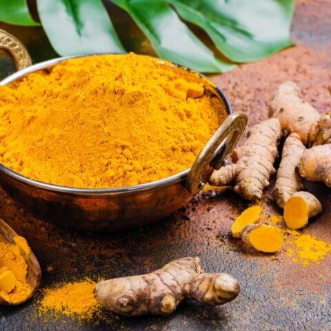 A bowl of ground turmeric with whole sliced turmeric rhizomes around it