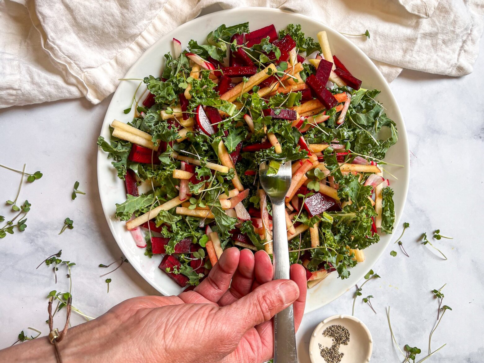 Red root kale salad plated with a fork and a small bowl of pepper off to the side.