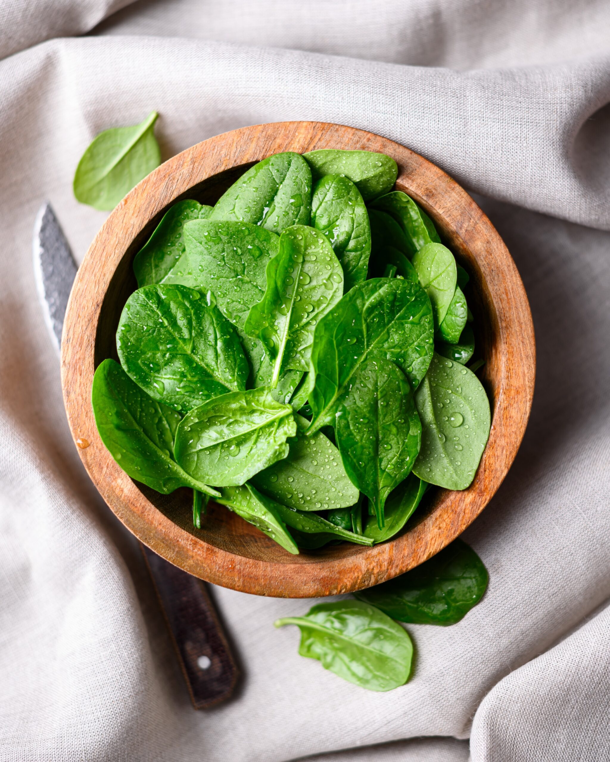 Spinach in a wooden bowl with a knife.