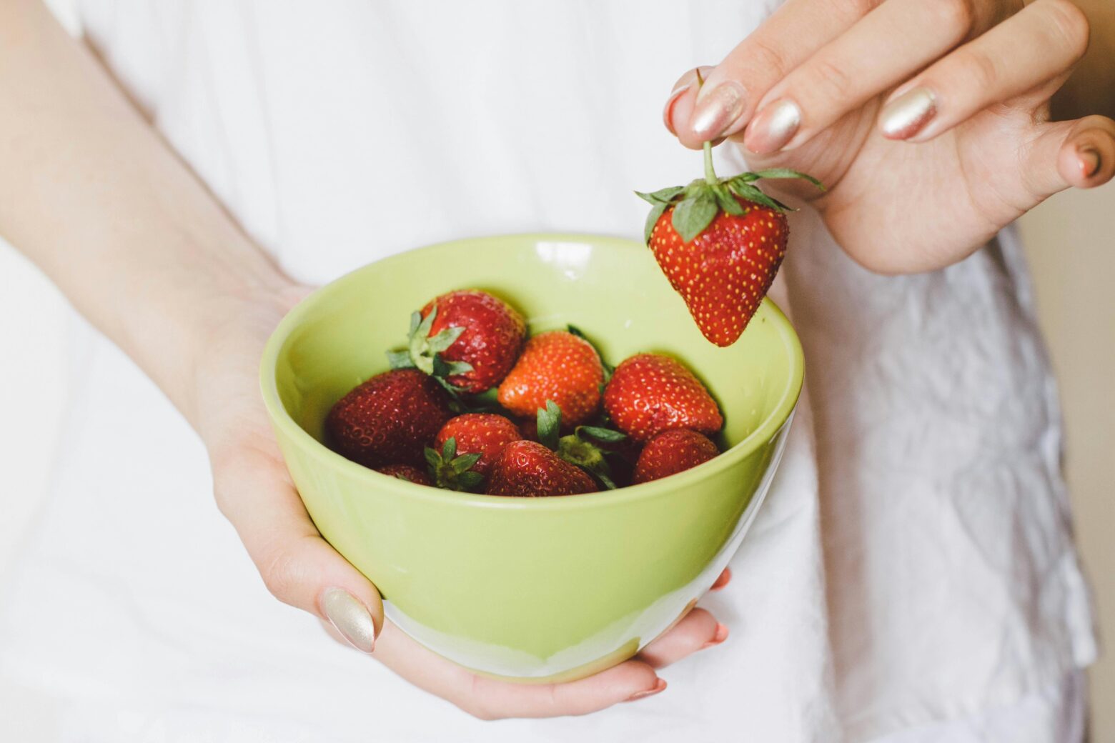 A lady picking up a strawberry from a bowl of strawberries.