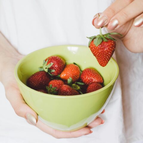 A lady picking up a strawberry from a bowl of strawberries.