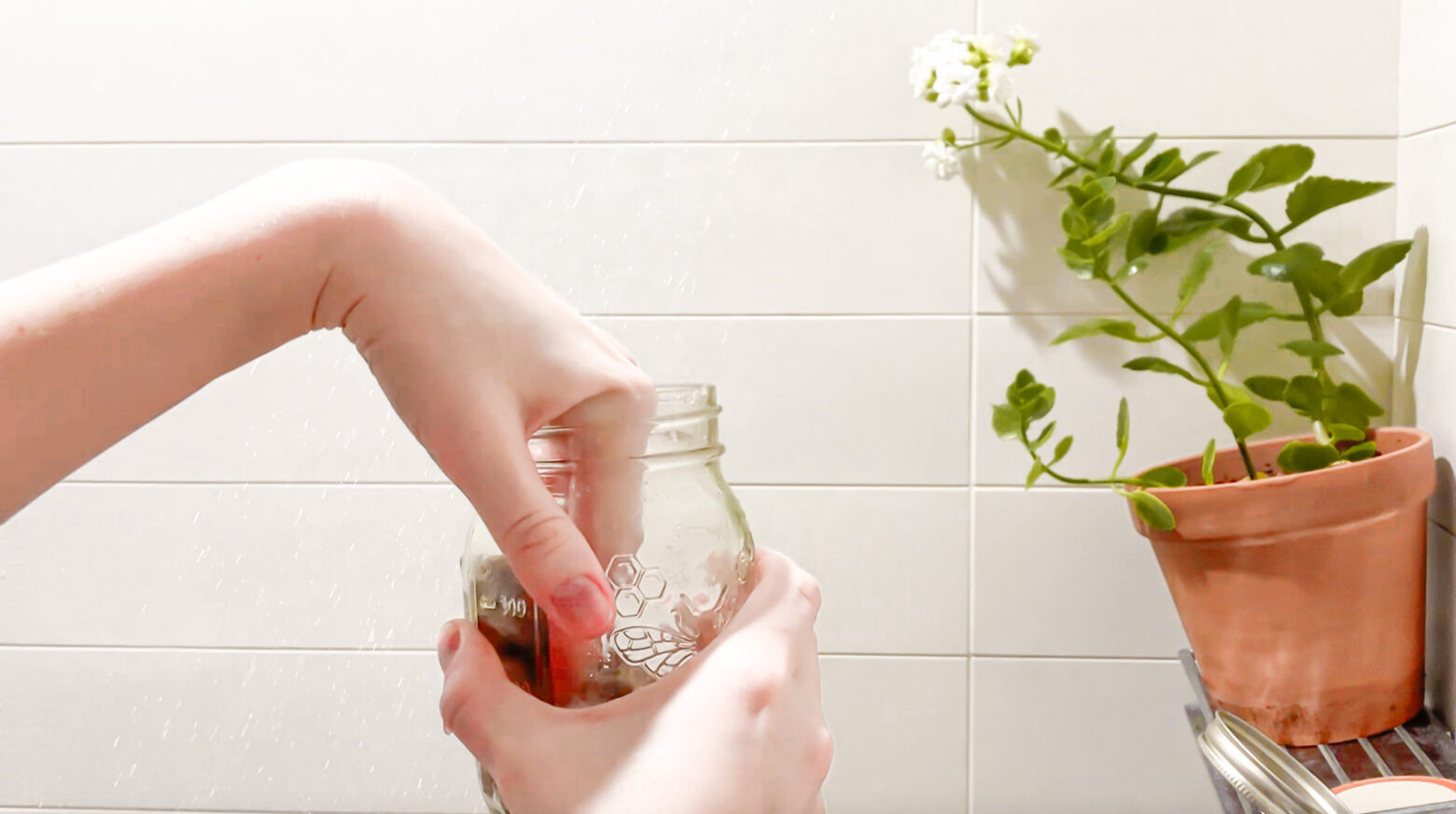 Exfoliating sugar scrub being taken out of a mason jar in the shower.