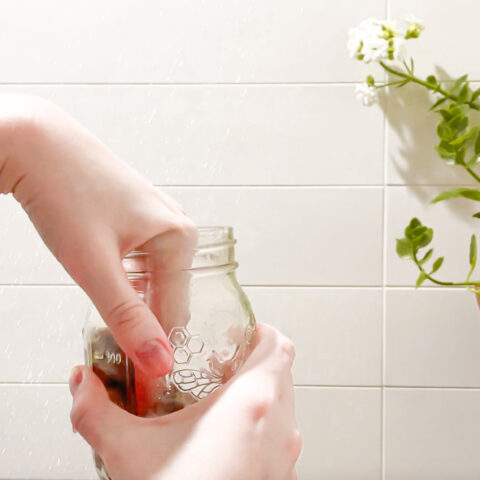 Exfoliating sugar scrub being taken out of a mason jar in the shower.