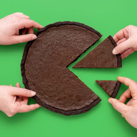 Different hands taking away different portion sizes of a circular brownie