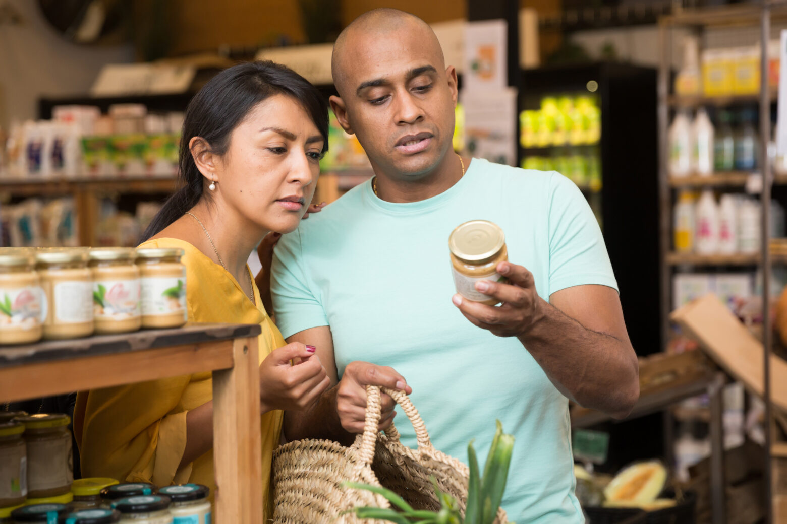 A couple grocery shopping and inspecting the label on a jar