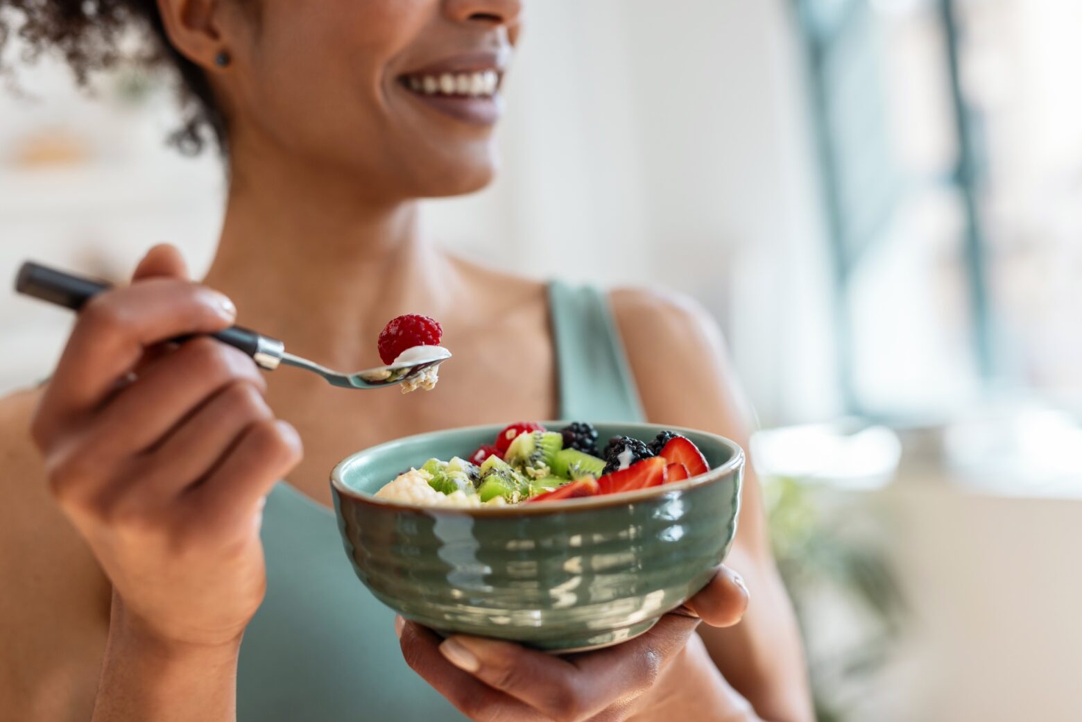 Women eating a bowl of fruit, smiling.