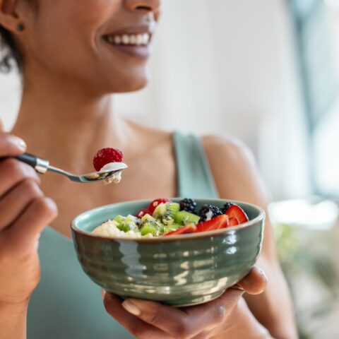 Women eating a bowl of fruit, smiling.