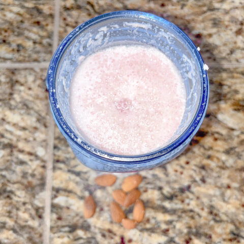 Raspberry almond milk from above on the counter with almonds.