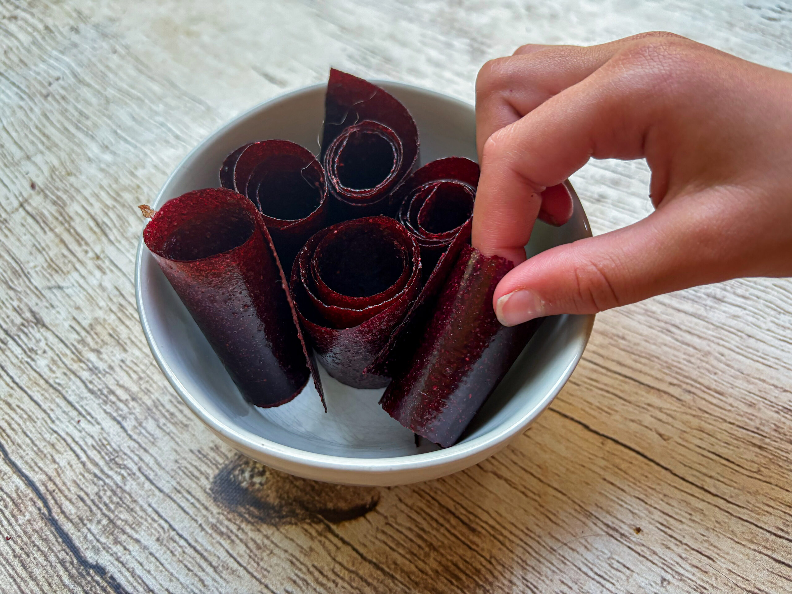 final photo of vegetable fruit roll-ups in a bowl with a hand grabbing them