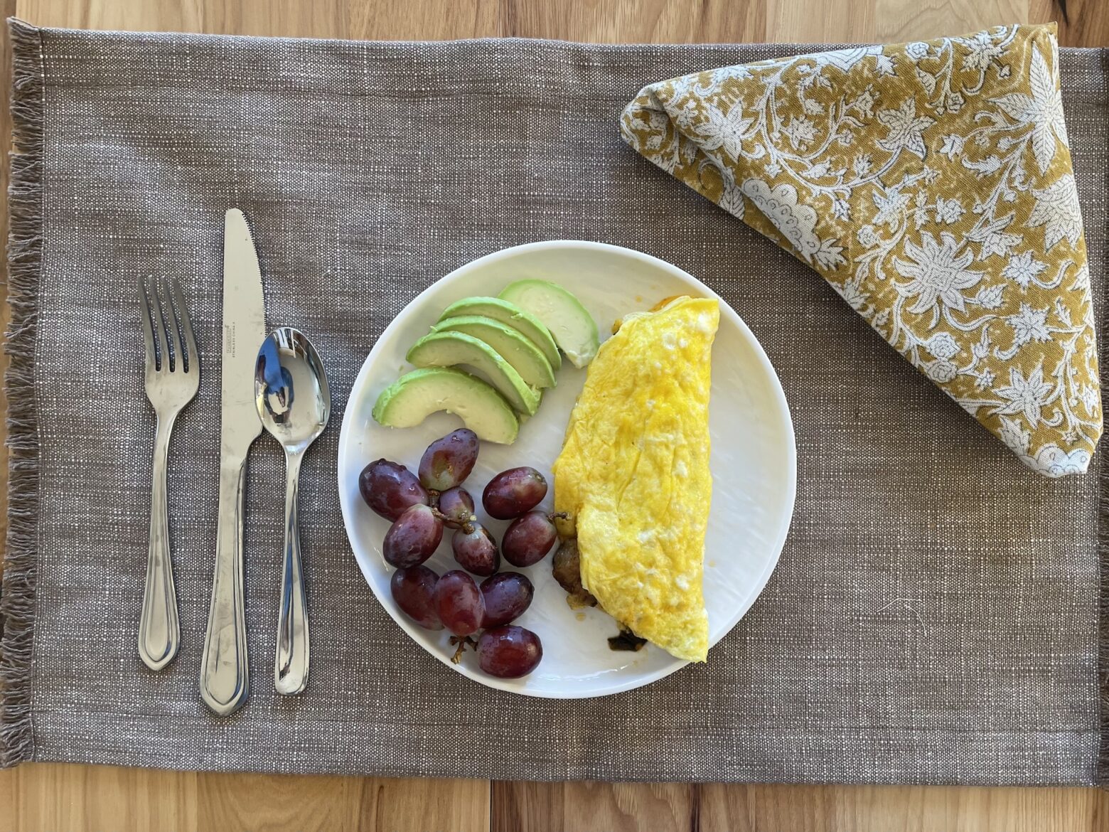 Western omelet finished on a table with grapes and avocado.