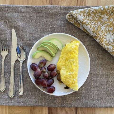 Western omelet finished on a table with grapes and avocado.