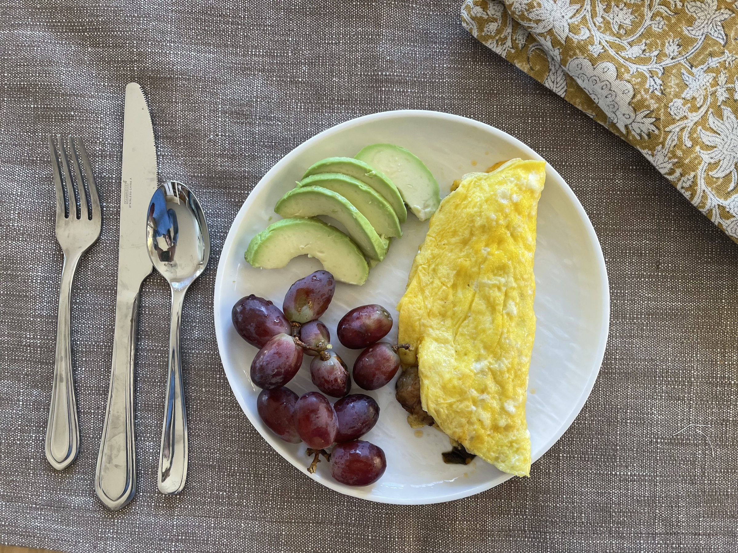 Close up of western omelet finished on a table with grapes and avocado. 