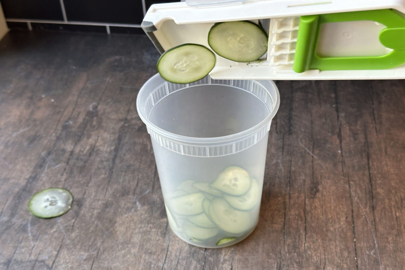 Using a mandoline to slice cucumber into a plastic container