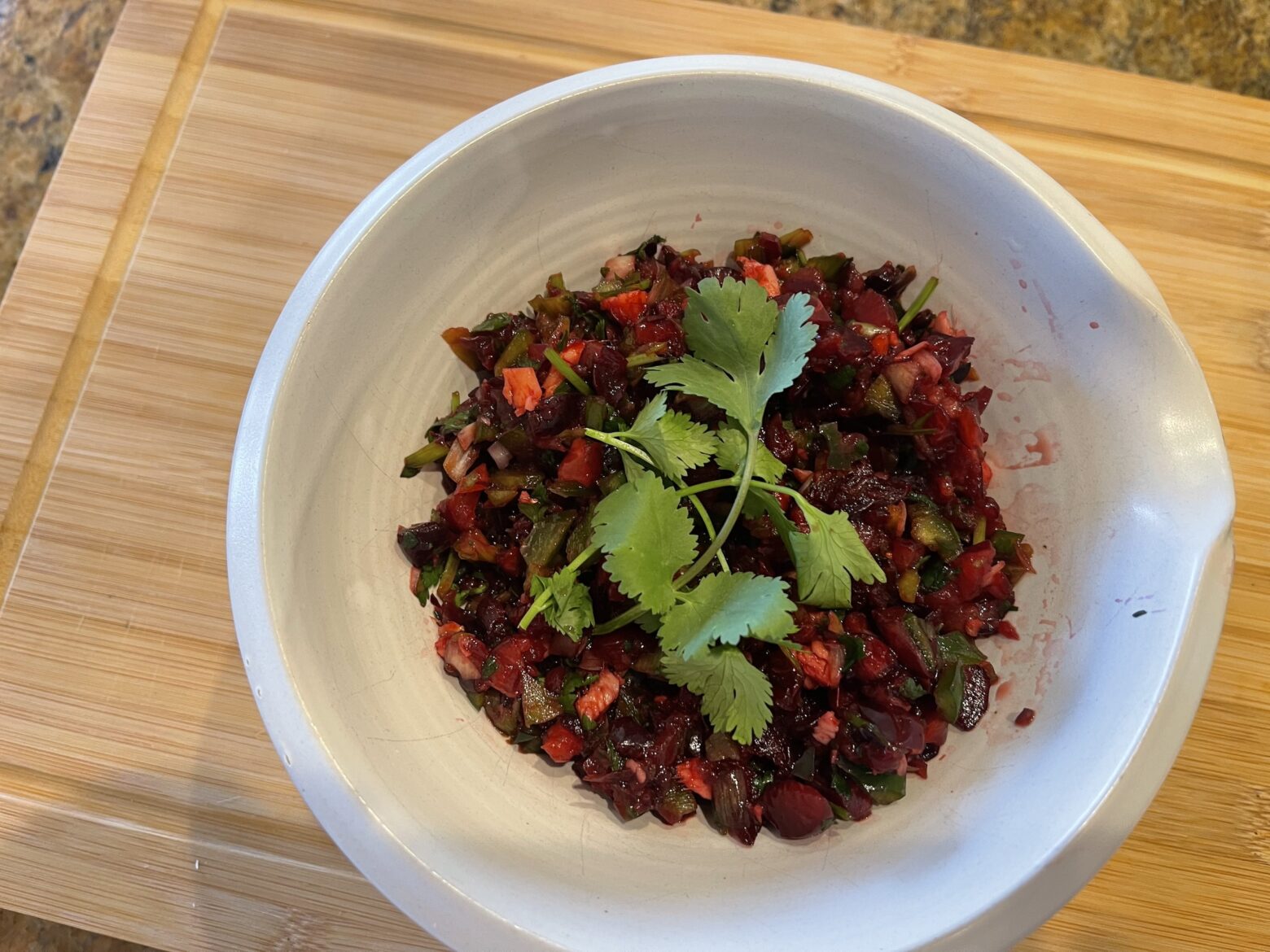 Cherry salsa finished in a bowl, sitting on a cutting board.