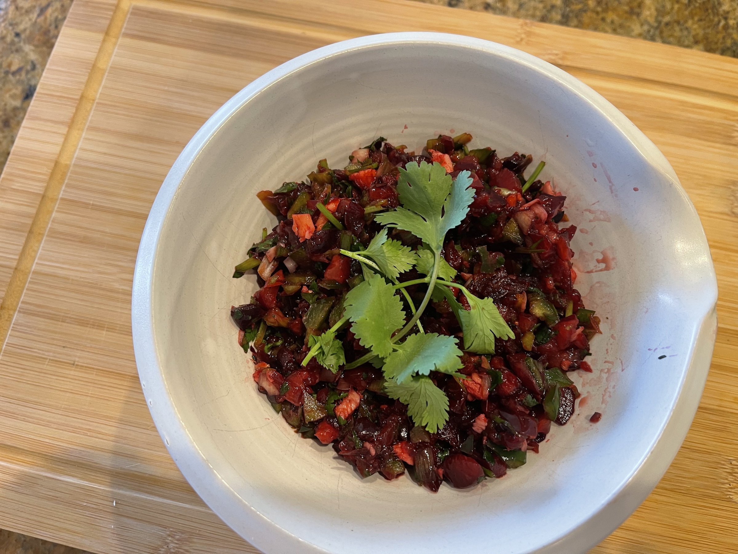 Cherry salsa finished in a bowl, sitting on a cutting board. 