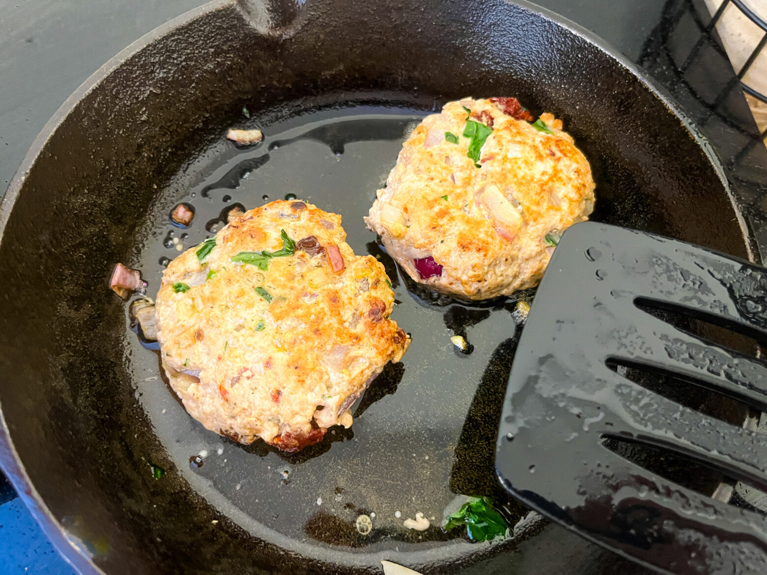 Spinach turkey burgers cooking in a cast iron pan over the stove.