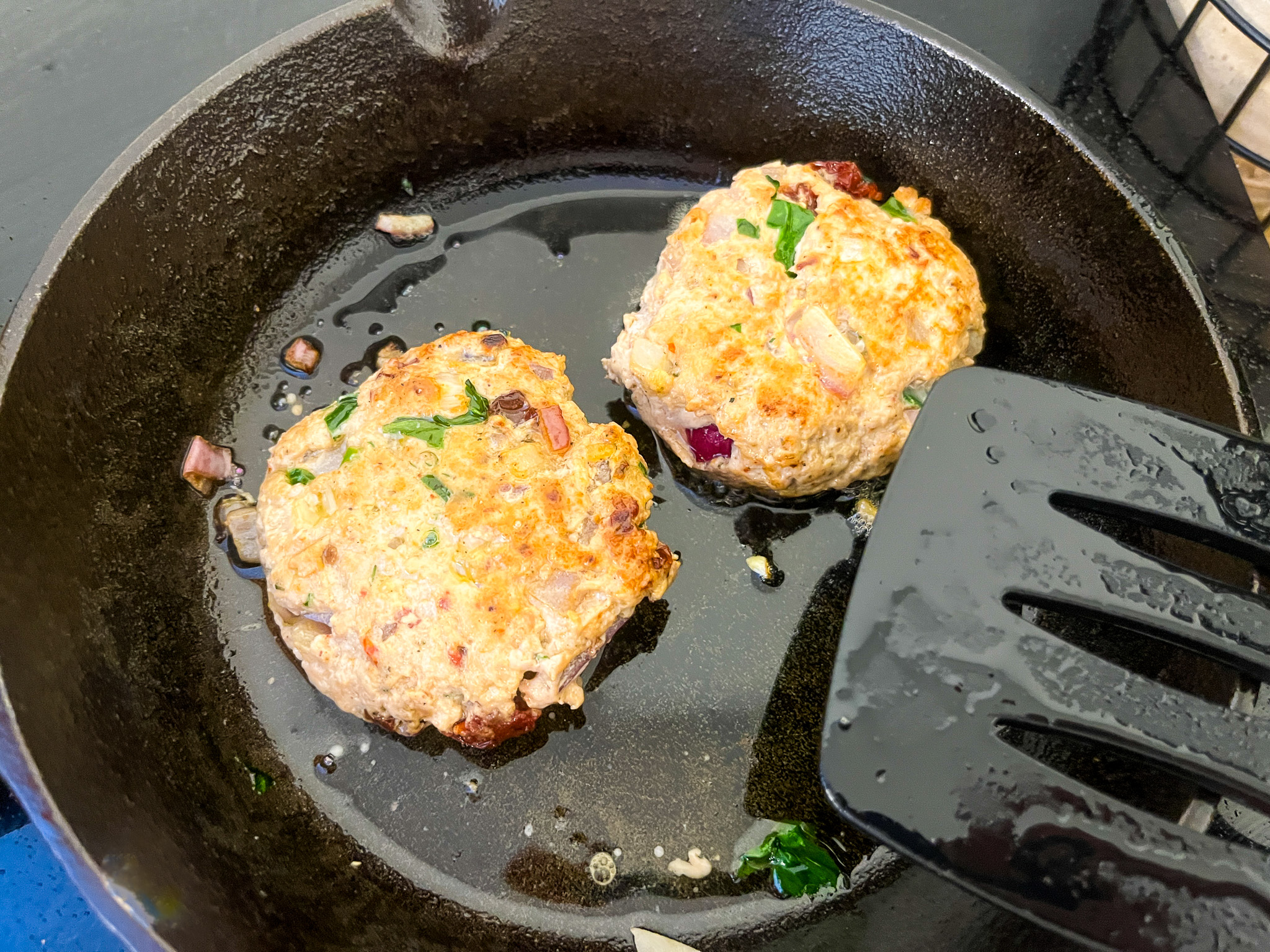 Spinach turkey burgers cooking in a cast iron pan over the stove. 