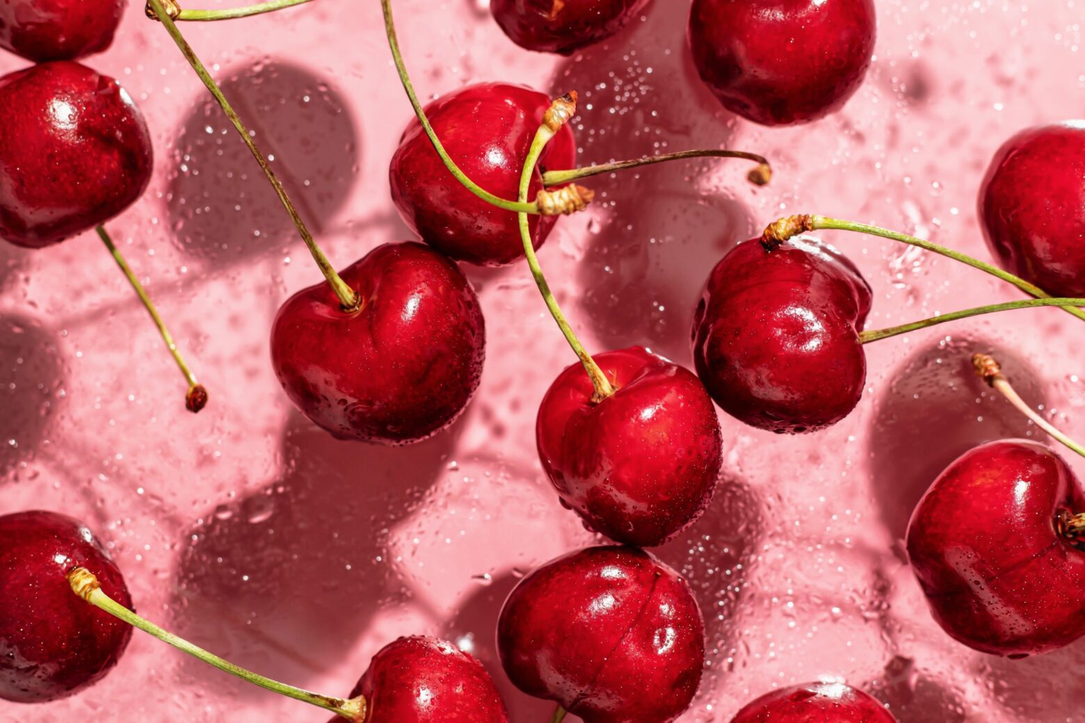 Fresh cherries floating in clear water over a pink background