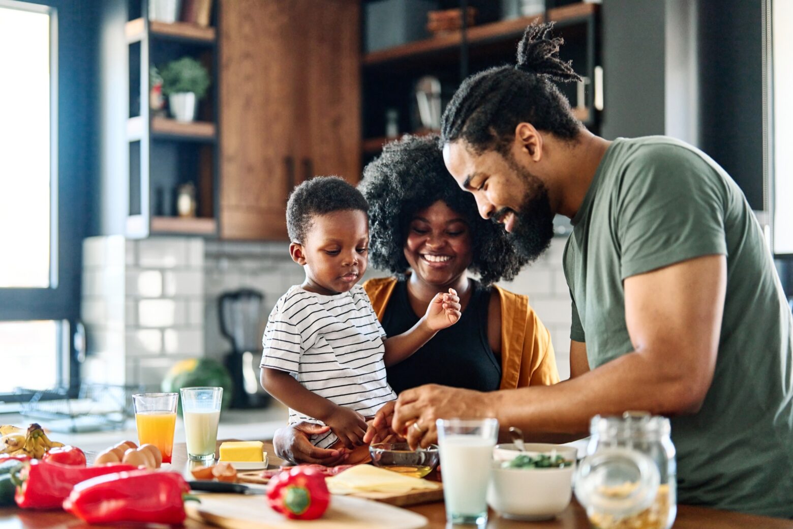 Two parents and their young child work on preparing a meal together in the kitchen