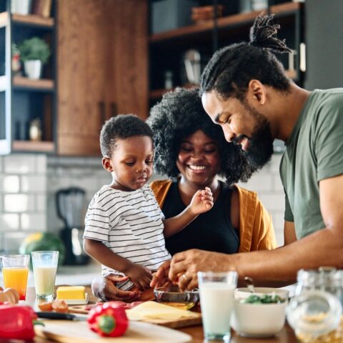 Two parents and their young child work on preparing a meal together in the kitchen