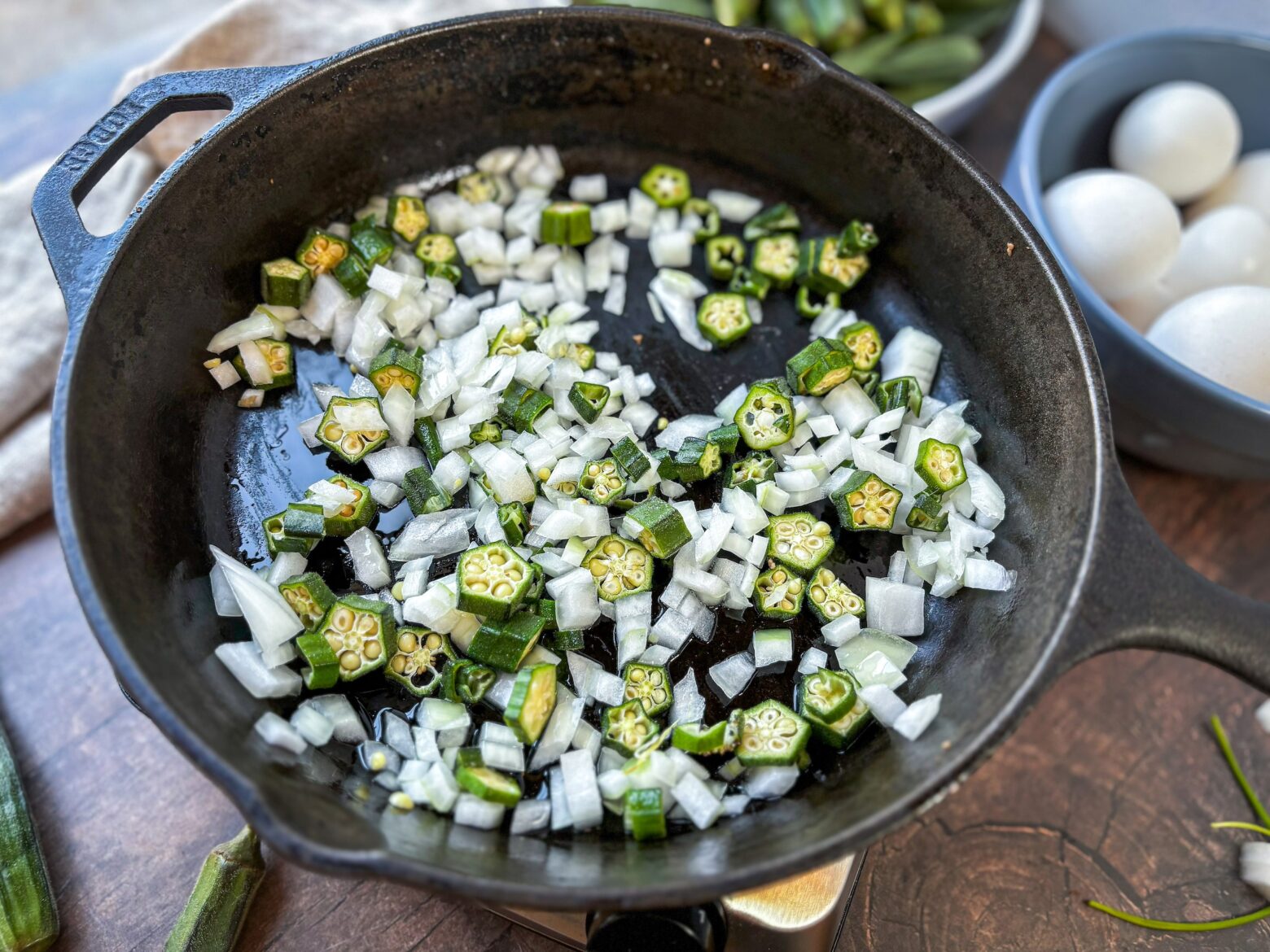 Okra and onion pieces cooking over the stove in a pan.