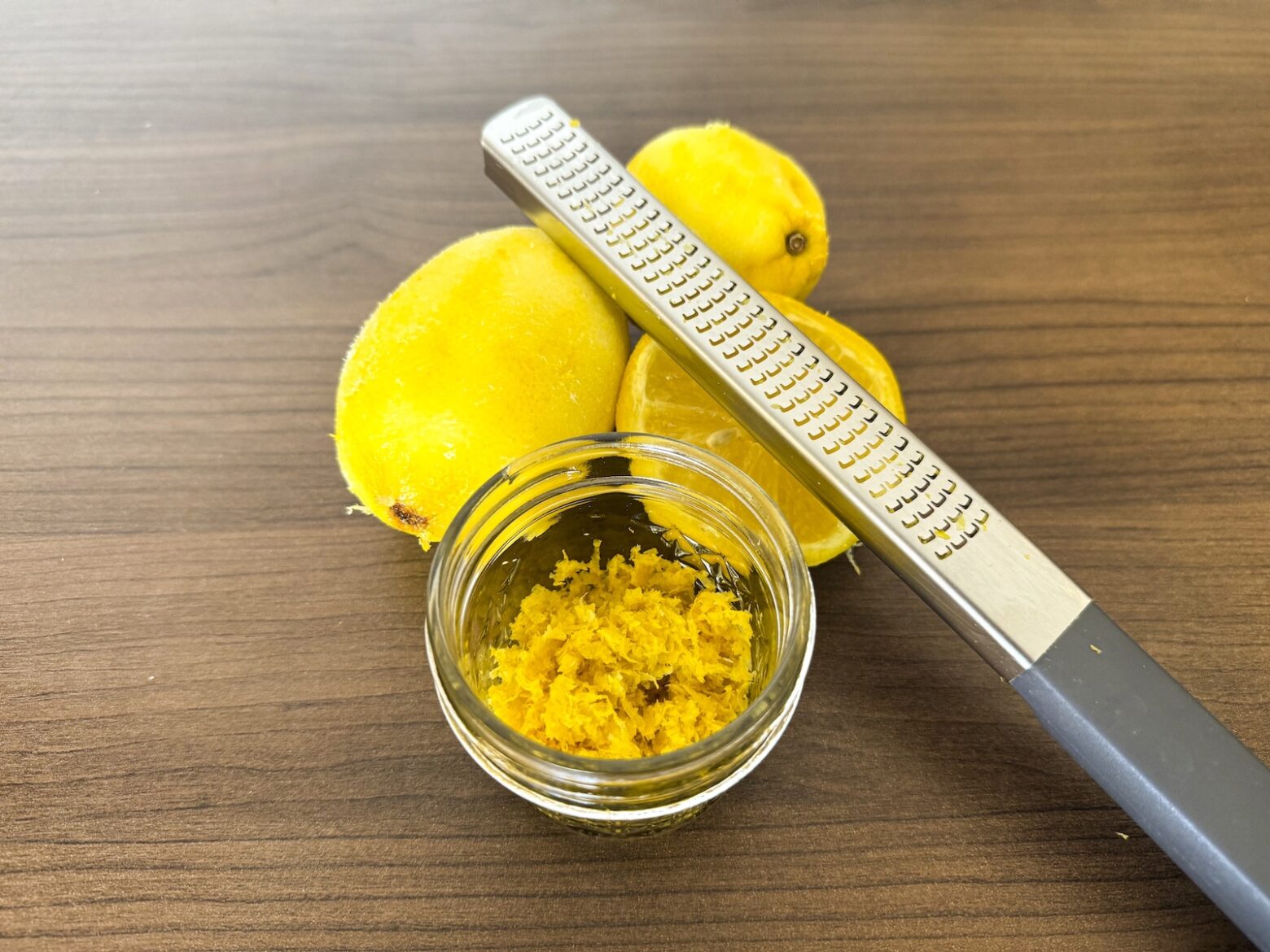 Prep photo of lemon zest in jar with grater and zested lemons behind jar