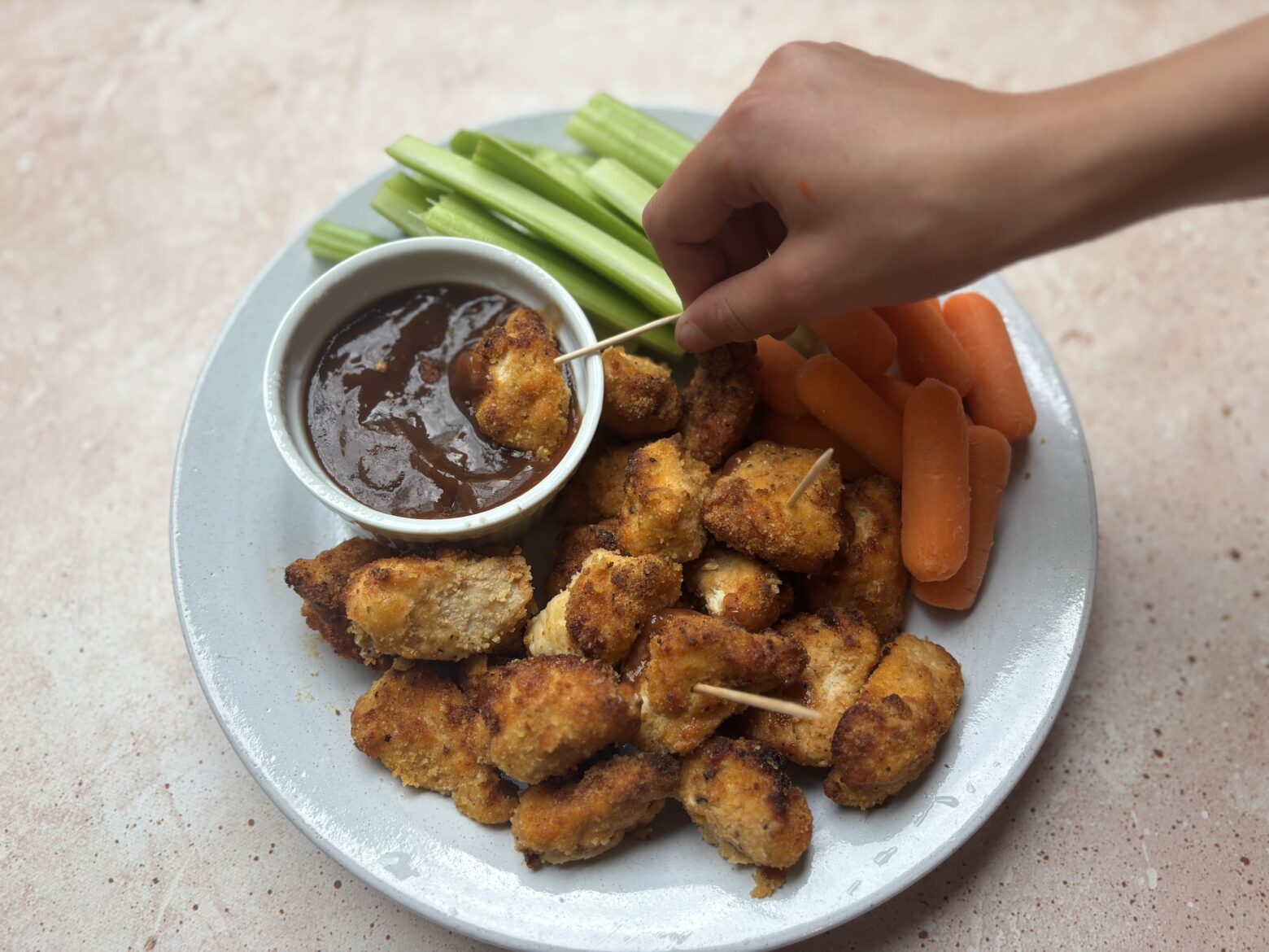 Baked chicken bites being eaten on a plate with veggies and BBQ sauce.
