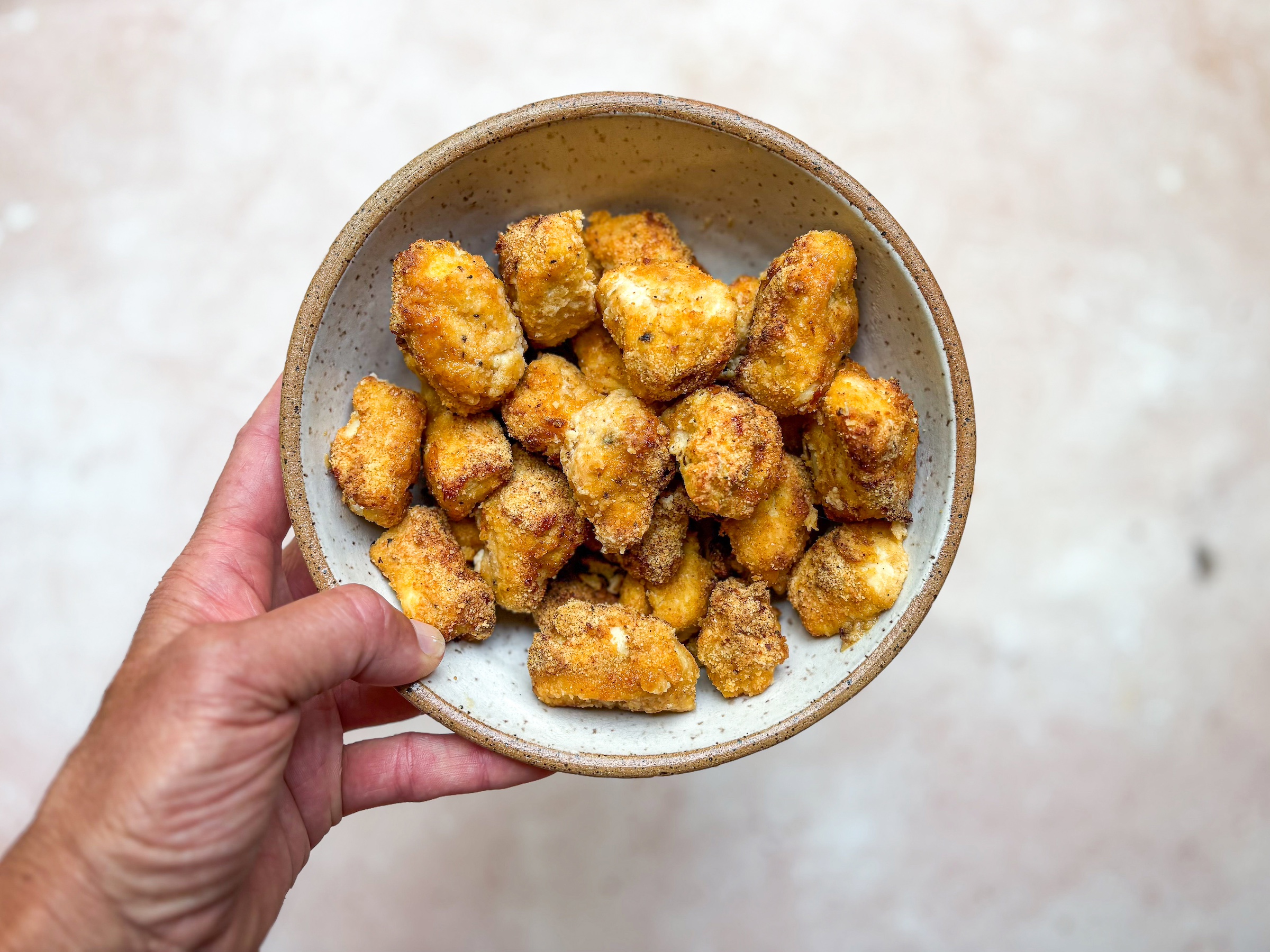 Baked chicken bites in a bowl being held by a hand. 