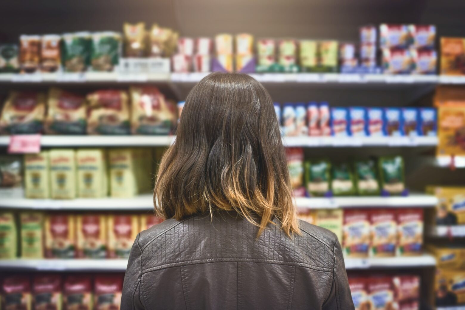 Rear view of a woman looking at a variety of packaged goods on the shelves of a grocery store.