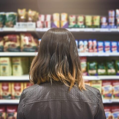 Rear view of a woman looking at a variety of packaged goods on the shelves of a grocery store.