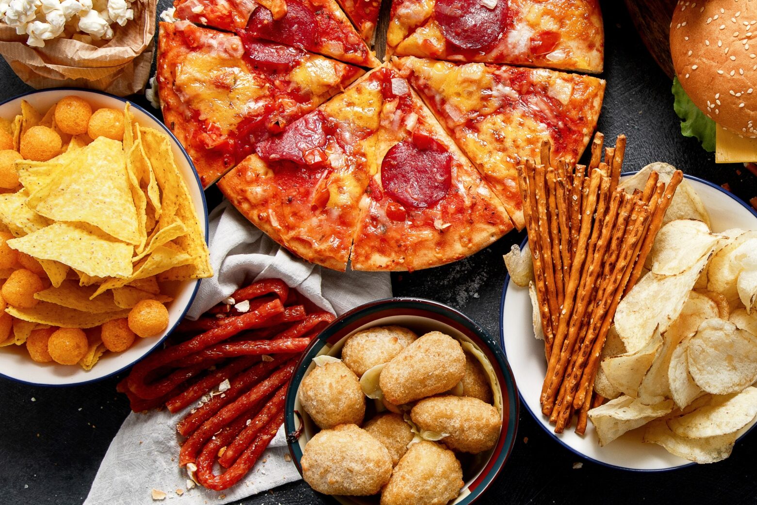 Above shot of ultra-processed junk foods that can contribute to metabolic disease, such as pizza, salty snacks, and jerky.