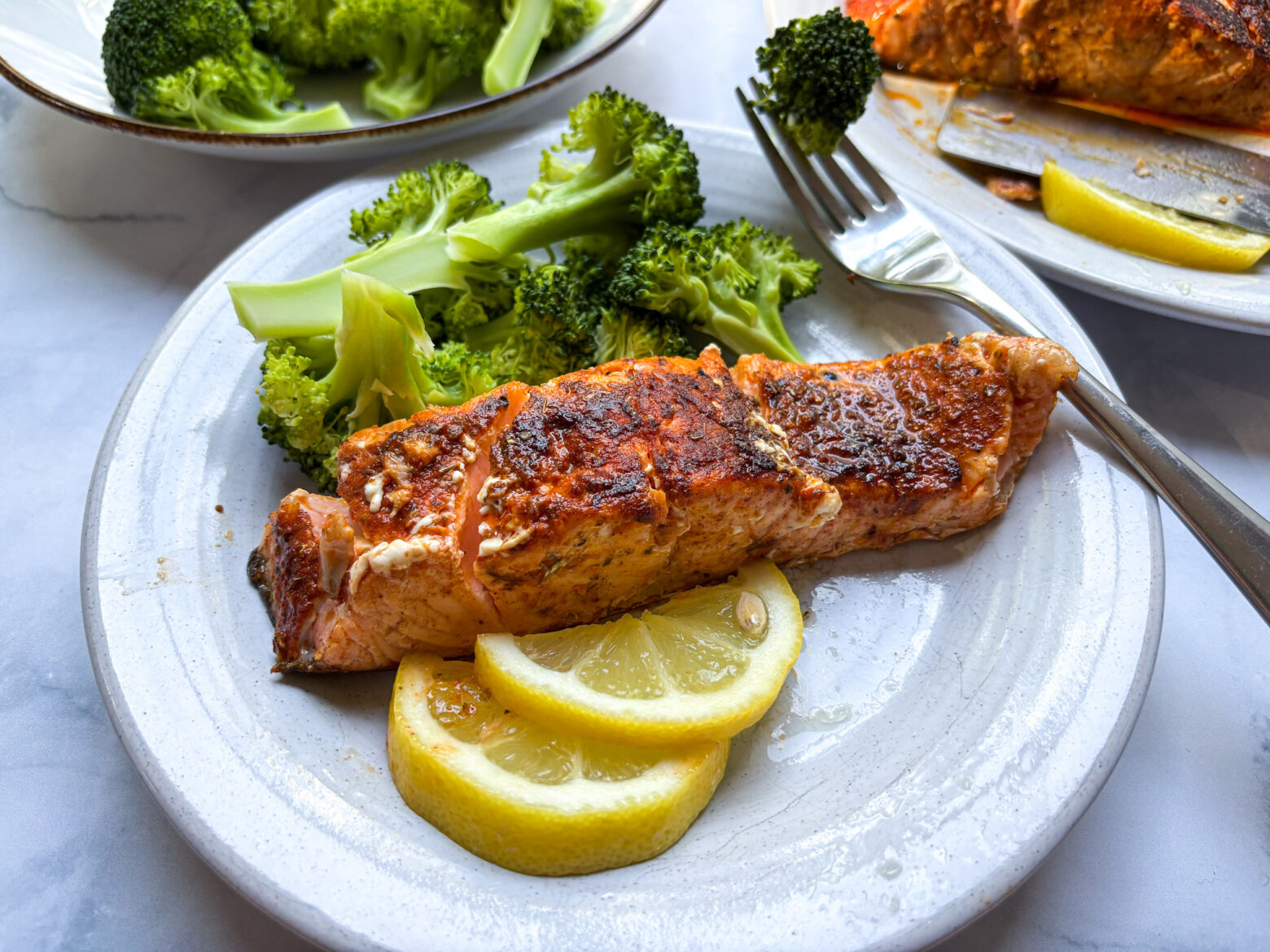 Blackened salmon finished, and plated with lemon slices and broccoli.