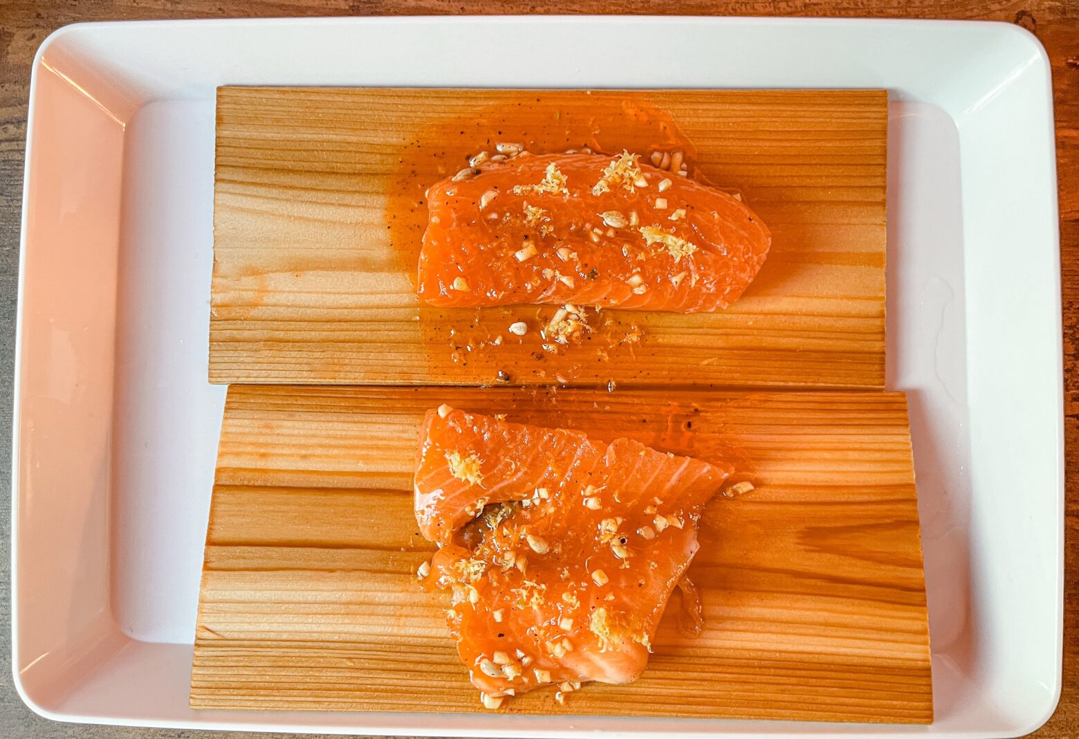 Cedar plank grilled salmon being prepped on the wooden boards with marinade.