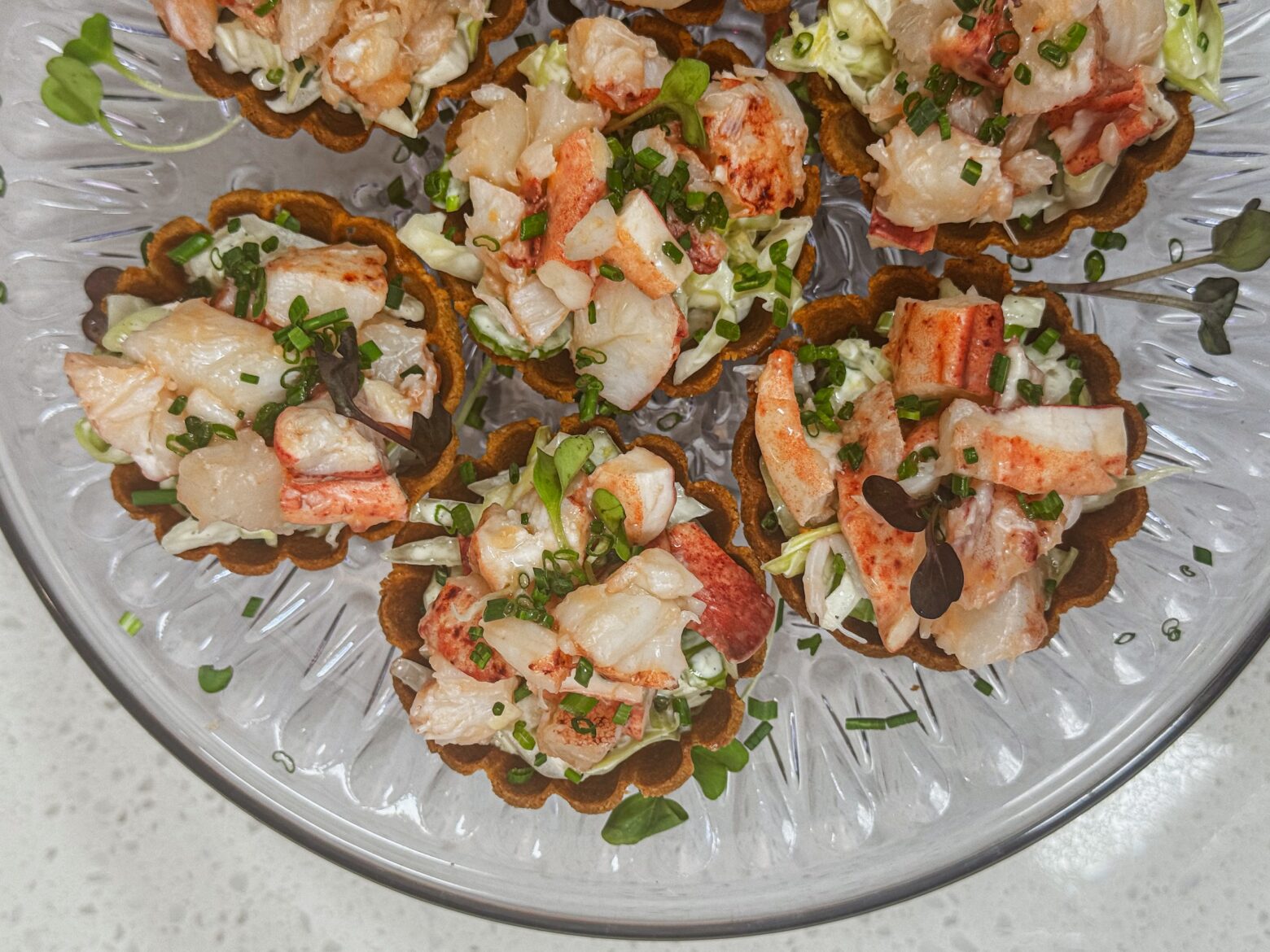 Lobster rolls finished on a clear platter, close up.